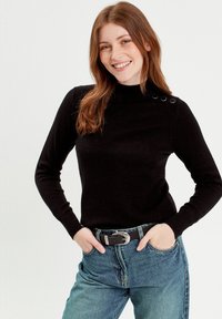 Sort turtle neck sweater med lange ærmer, præsenterer dekorative knapdetaljer på den ene skulder. Sammen med højtaljede blå jeans.