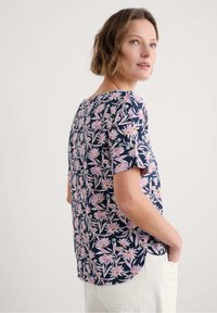 Marineblaues T-Shirt mit kurzen Ärmeln, bedeckt mit einem pink-weißen Blumenmuster, mit rundem Ausschnitt und seitlichen Schlitzen für zusätzlichen Komfort.