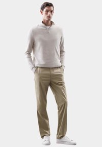 Suéter de cuello con cremallera color beige claro combinado con pantalones chinos color tostado y zapatillas blancas. El suéter tiene mangas largas y una textura suave.