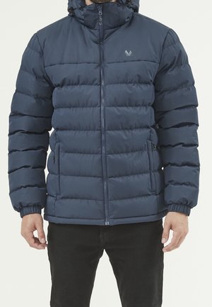 Mężczyzna ubrany w ciemnoniebieską pikowaną kurtkę puchową z przednim zamkiem błyskawicznym, zapinanymi kieszeniami po bokach oraz elastycznymi mankietami, widziany od klatki piersiowej do bioder.