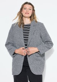 Sako v houndstooth vzoru v černé a bílé barvě, s volným střihem, klopovými límci, dvěma předními kapsami a zapínáním na dva knoflíky.
