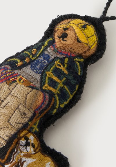 Porte-clés en tissu brodé en forme d'ours portant un chapeau jaune, une veste bleu marine et un pantalon beige avec une couture colorée et complexe.