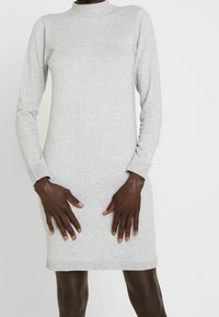 Abito di maglia grigio con maniche lunghe, collo alto e polsini a coste. Texture liscia e lunghezza fino al ginocchio, caratterizzato da un design semplice e classico.