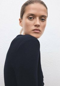 Tmodrý žebrovaný svetr s vypasovaným střihem a texturovanou tkaninou, s kulatým výstřihem a dlouhými rukávy.