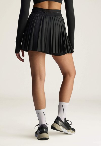 Falda deportiva negra con plisados y una cinturilla alta, combinada con calcetas blancas y zapatillas deportivas negras con un acento gris.