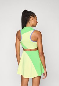 Σετ αθλητικής κορυφής κομμένης σε πράσινο και κίτρινο με φούστα, με αντίθετη γαλάζια επένδυση, που διαθέτει σχεδιασμό με ψηλό λαιμό και εφαρμοστό μπούστο. Λείο υφή.