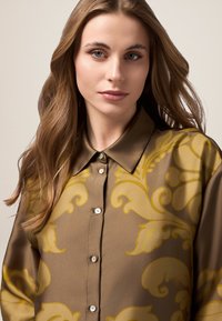 Chemise marron avec un motif floral jaune, fermeture à boutons sur le devant et col. Texture douce avec un léger éclat.
