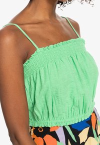 Vihreä, teksturoitu puuvillapaita ohutolkaimilla ja smokkikirjonnalla kauluksessa ja vyötäröllä, yhdistetty värikkään kuviollisen hameen kanssa.