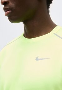 Close-up of a person wearing a light yellow Nike sports shirt with a gray swoosh logo on the chest.