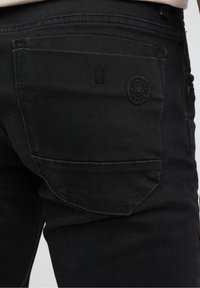 Jeans in denim nero con una tasca posteriore con dettaglio del logo in rilievo e una finitura leggermente testurizzata. Linee pulite con cuciture minime.
