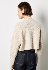 Suéter crema recortado con patrón de diamantes texturizado, cuello con canalé y hombros caídos. Combinado con pantalones de mezclilla oscuros de talle alto.