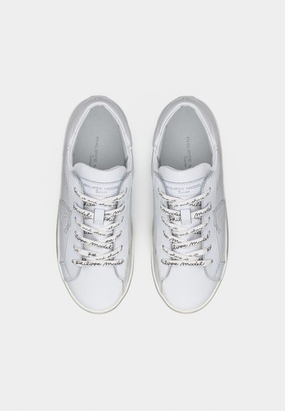 Άσπρα δερμάτινα αθλητικά παπούτσια με κορδόνια που φέρουν εκτυπωμένο κείμενο, με στρογγυλεμένη μύτη και διακριτικές λεπτομέρειες με λογότυπο στα πλαϊνά και στη γλώσσα του παπουτσιού.