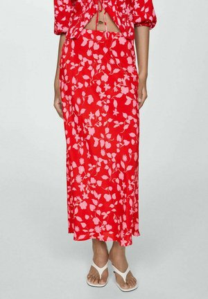 Červená midi sukňa s kvetinovým vzorom, na ktorej sú ružové kvety a listy, vzdušný materiál, vysoký pás, skombinovaná s bielymi plochými sandálmi.