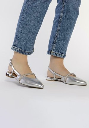 Zapatos planos metálicos plateados con punta afilada, que presentan una correa decorativa adornada con strass y un tacón delgado.