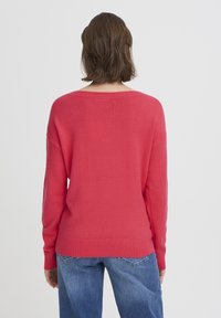 Pull-over rouge avec un large col, manches longues, poignets et ourlet côtelés. Texture douce, coupe décontractée, design minimaliste.