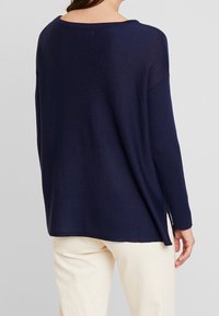 Navy blue sweter dzianinowy ma szeroki dekolt, długie rękawy i boczne rozcięcia. Materiał jest miękki, a rękawy mają prążkowany wzór.