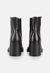 Botas de cuero negro hasta el tobillo con un tacón texturizado, cremalleras laterales y un acabado suave, que cuentan con una punta redondeada y un tacón cuadrado de altura media.