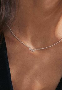 Silverhalsband med en delikat kedja och ett hängsmycke som har texten "Lycka". Designen är minimalistisk med tydlig skrift.