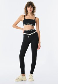 Czarny zestaw sportowy składający się z krótkiego topu z logowaną tasiemką oraz legginsów z wysokim stanem z kontrastowym paskiem; gładki, elastyczny materiał.