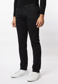 Zwarte katoenen broeken met een slim fit, voorzien van een vlakke voorkant, zijzakken en een enkele knoopsluiting, gecombineerd met witte sneakers.