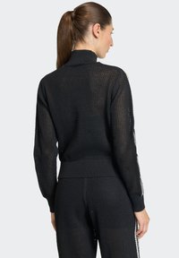 Crni pleteni džemper s mrežastim uzorkom, visokim ovratnikom i rebrastim manšetama, koji ima prianjajući kroj i duge rukave.