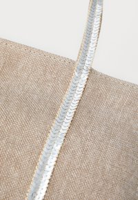 Bežna tkaninska torba s teksturiranom površinom, s sjajnim srebrnim aplikacijama od šljokica duž naramenice kao dekorativni detalj.