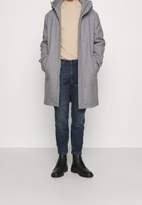 Grå ullblandning kappa med huva, beige polotröja, blå denimjeans och svarta läderstövlar. Flat och strukturerad design med dolda stängningar.
