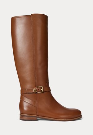 Botte d'équitation haute en cuir marron avec un petit talon empilé et un détail de boucle dorée autour de la cheville sur fond blanc uni.