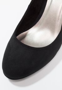 Chaussure à talon haut en suede noir avec un bout arrondi et une doublure intérieure lisse et argentée. Design minimaliste avec une silhouette épurée.