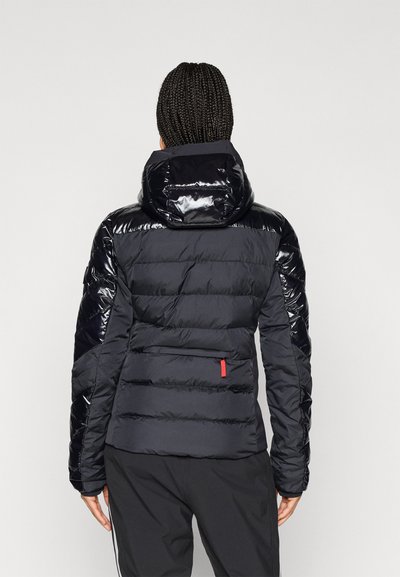 Μαύρο μπουφάν με γυαλιστερή κουκούλα και ώμους, διαθέτει φερμουάρ με κόκκινη λεπτομέρεια και σχεδίαση καπιτονέ. Λείος υφασμάτινος ιστός.