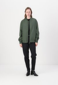 Groene bomberjack met een ritssluiting, geribbelde manchetten en onderkant. Draag het over een zwarte top, gecombineerd met zwarte jeans en elegante zwarte enkellaarsjes.