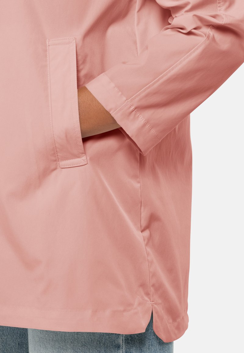 Helle rosa wasserdichte Jacke mit lockerer Passform, die über eine Seitentasche und hochgerollte Ärmel verfügt, hergestellt aus glattem, glänzendem Stoff.