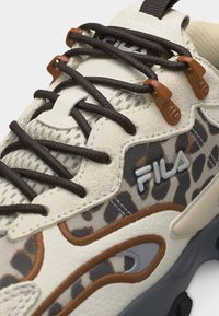 Gros plan sur une basket FILA beige et marron avec imprimé léopard, lacets marron et crochets en tissu sur la tige texturée et la semelle.