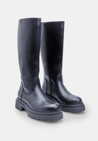 Pár vysokých čiernych kožených botas s hrubými podrážkami a bočnými zipsami, vystavené na bielom pozadí.