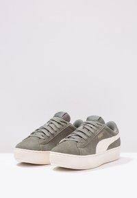 Sneaker basse in suede grigio con dettagli bianchi, linguetta in mesh testurizzato e lacci piatti. La suola in gomma presenta scanalature orizzontali per una migliore presa.