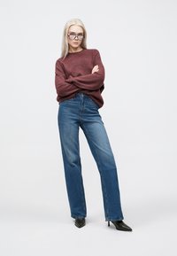 Maroon knit sweater with loose sleeves paired with high-waisted, straight-leg blue jeans and pointed black heels. Light background.