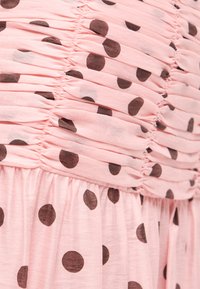 Ροζ ύφασμα με μεγάλα μαύρα πουά, με πιετά σχέδια ραφών που δημιουργούν οριζόντιες υφασμάτινες γραμμές.