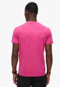 T-shirt a maniche corte in cotone rosa brillante con collo rotondo classico e una texture liscia; la vista posteriore rivela un design semplice e privo di motivi.