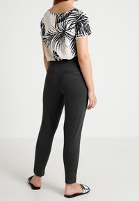 Avskuren vit topp med svart palmlövsmönster, i kombination med smala grå leggings. Svarta sandaler med silverdetaljer, sedd från baksidan.