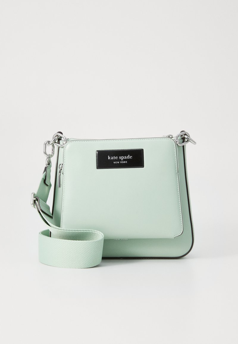Borsa a tracolla in pelle verde menta con chiusura a zip, tracolla regolabile e placca con logo nera. Presenta una texture liscia e un design minimal.