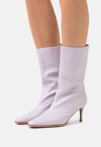 Botas de cuero lavanda hasta el tobillo con un diseño arrugado, punteras puntiagudas y un delgado tacón de aguja. Textura suave con un detalle mínimo.