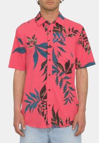 Camisa de manga corta rosa con patrones de hojas en azul y negro, cierre de botón y bolsillo en el pecho. Tela suave con un corte relajado.