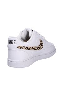White leather sneakers featuring a textured leopard print Swoosh and black "NIKE" logo on the heel. White rubber sole with a speckled design.