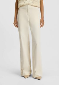 Beige wijde broek met een gladde textuur, hoge taille en een voornaaddetail, gecombineerd met puntige beige hakken.