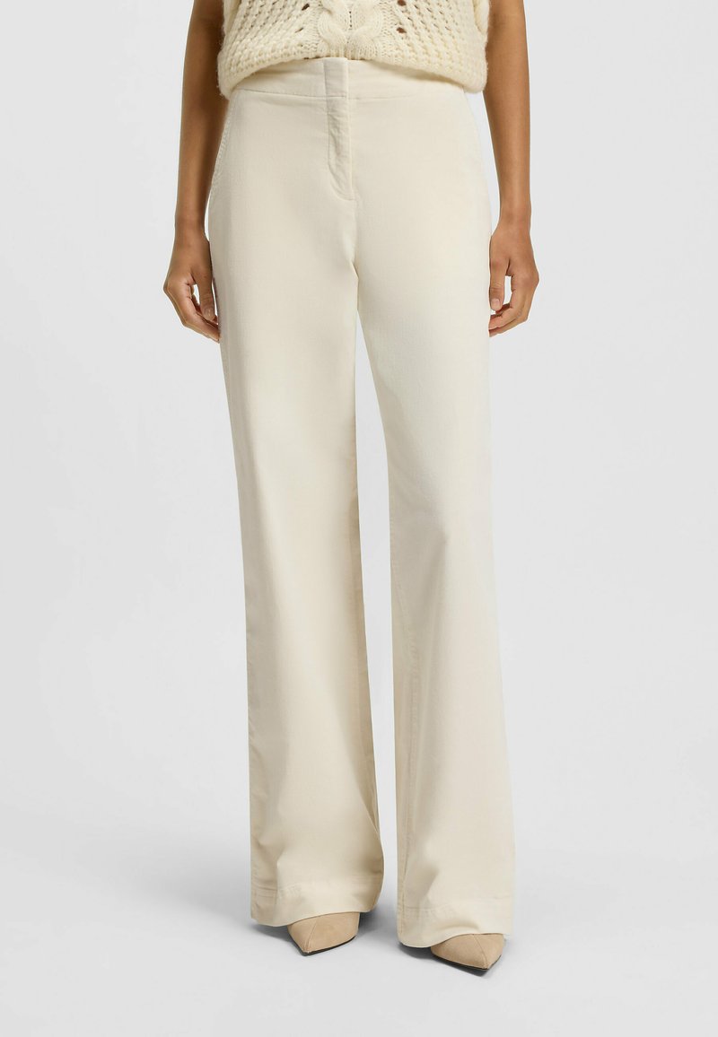 Beige wijde broek met een gladde textuur, hoge taille en een voornaaddetail, gecombineerd met puntige beige hakken.