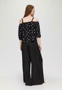 Top nero off-the-shoulder con motivi astratti bianchi, maniche a sbuffo e spalline regolabili, abbinato a pantaloni neri a gamba larga in un tessuto liscio.