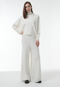 Witte gebreide coltrui met een naadloos ontwerp, gecombineerd met brede pantalons in bijpassende stof, met een zachte textuur en een relaxte pasvorm.