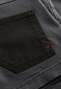 Tissu gris avec une poche sombre ornée de détails en point de croix rouges. Les textures sont lisses et finement tissées, présentant des variations subtiles de couleur.