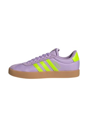 Zapatilla Adidas lavanda con rayas amarillas neón y lengüeta en el talón, suela marrón y diseño con cordones, vista lateral sobre fondo blanco.