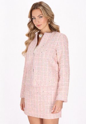 Giacca in tweed rosa con un motivo testurizzato, caratterizzata da un design senza colletto e due tasche frontali, abbinata a una minigonna coordinata.